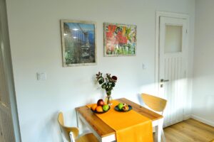 stolik a na nim pomarańczowy bieżnik, kwiaty i owoce, obrazy nad stołem