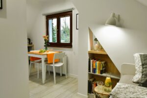 jasny pokój z łóżkiem i stolikiem na którym jest pomarańczowy bieżnik i kwiaty