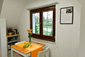 drewniany stolik z pomarańczowym bieżnikiem, kwiatami i owocami ustawiony przy oknie