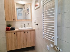 łazienka z lustrem i kaloryferem, obok umywalki ręczniki zwinięte w rulon