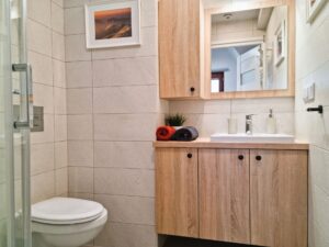 łazienka z drewnianymi meblami i lustrem, obok umywalki ręczniki zwinięte w rulon