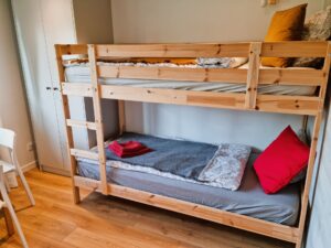 łóżko dwupoziomowe z kolorowymi poduszkami, obok szafa