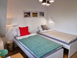 dwa zaścielone łóżka jednoosobowe, nad nimi 3 obrazy gór