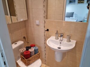 mała łazienka z lustrem i umywalką, na toalecie koszyk ze zwiniętymi w rulon ręcznikami